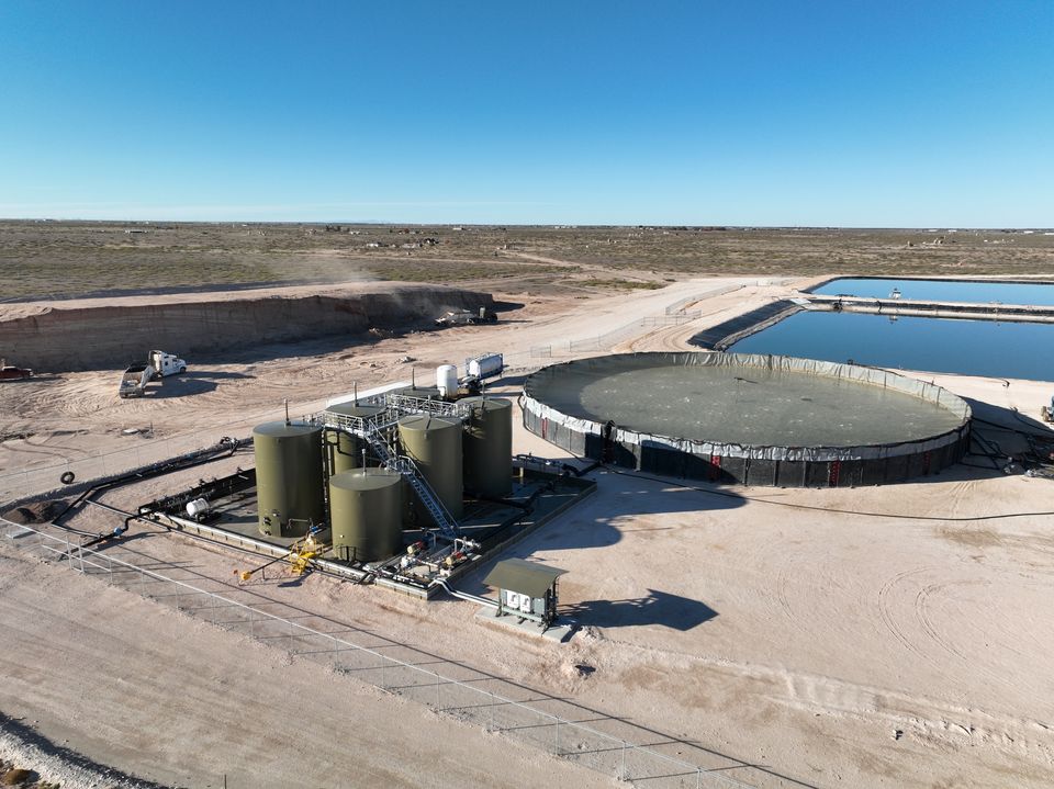 Drone view of the facility tank battery beside a circular above-ground storage tank and ponds